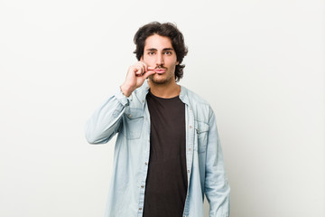 Young handsome man against a white background with fingers on lips keeping a secret.