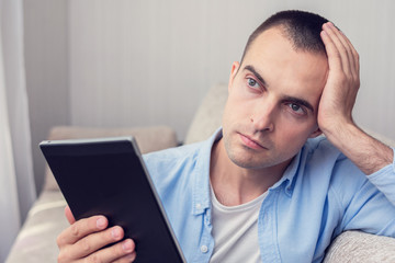 Guy reading an e-book sitting at home, portrait, toned