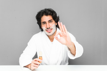 Young man shaving his beard cheerful and confident showing ok gesture.