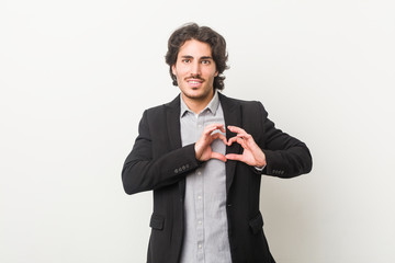 Young business man against a white background smiling and showing a heart shape with hands.