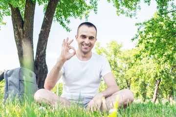 Naklejka na ściany i meble Happy man showing ok sign, guy sitting in Park in summer, portrait, toned