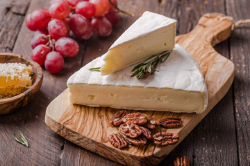 Segment of Brie cheese or soft cow's - French camembert  on wooden board with  grapes, honeycomb and pecan nuts.
