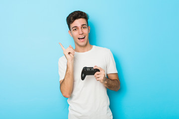 Young caucasian man playing videogames with game controller smiling cheerfully pointing with forefinger away. © Asier