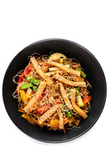 Sliced grilled pork, noodles in sauce, vegetables and sesame seeds in a black plate isolated on white background, top view