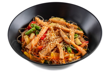 Sliced grilled pork, noodles in sauce, vegetables and sesame seeds in a black plate isolated on white background, side view
