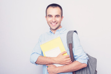 European student man with workbooks wearing backpack over grey background, portrait, toned, copy space