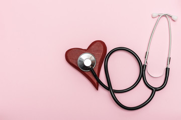 Fototapeta premium Flat lay overhead of red wooden heart and medical stethoscope on pink pastel background. Heart diseases prophylaxis and diagnostic concept. Health care concept.