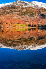 Fototapeta na wymiar Ullswater lake with snow capped mountains surrounding the second largest lake in the Lake District, Cumbria, UK. Autumn lake reflections on a peaceful day with still waters. 