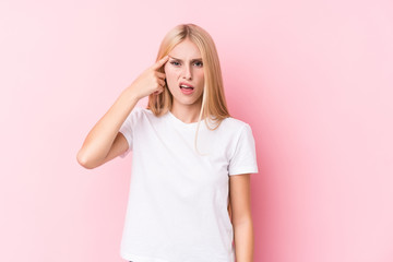Young blonde woman on pink background showing a disappointment gesture with forefinger.
