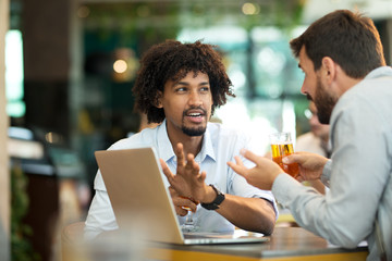 Young businessmen siting pub and drinking beer as they work