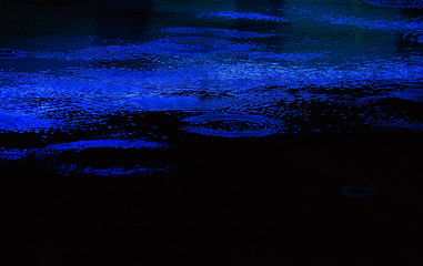 Rain drops falling into water lit by blue lights