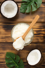 Coconut oil in the wooden spoon and glass jar on the brown wooden background. Natural product. Top view. Location vertical.