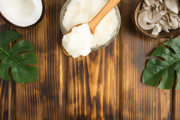 Coconut oil in the wooden spoon and coconut crisps on the brown wooden background. Natural product. Top view. Copy space.
