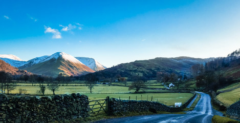 Scenic road in the Ullswater valley, Lake District, Cumbria, UK. Surrounded by snow capped peaks on a frosty cold winter day. 