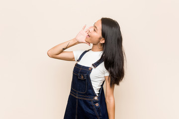 Young cute chinese teenager Young blonde woman wearing a coat against a pink background shouting and holding palm near opened mouth.