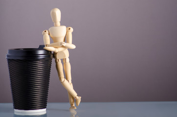 wooden man figure with cardboard cup of coffee on gray background
