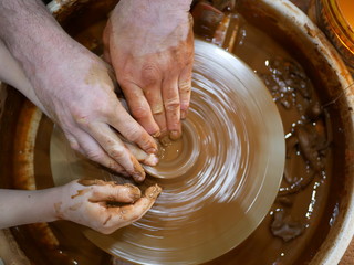 The master Potter teaches the child to make a clay jug on a modern Potter's wheel with an electric drive. The hands of a child and an adult man are stained with clay. Teaching pottery.
