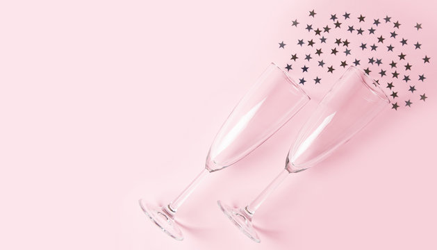 Two champagne glasses on pink background with confetti. Flat lay, top view, copy space.