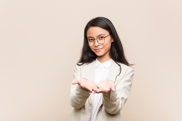 Young business chinese woman holding something with palms, offering to camera.