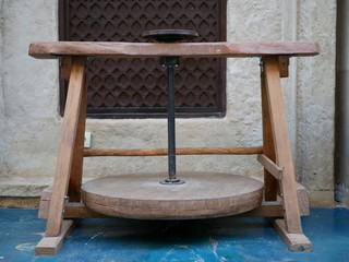 The old wooden foot-operated Potter's wheel in the background of the gray stone wall with a window.
