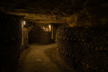 Fototapeta na wymiar Pathway in catacombs. Old skulls and bones form walls. Grim lighting. Underground cemetery