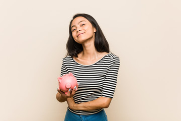 Young asian woman holding a piggy bank laughing and having fun.