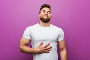 Young handsome caucasian man touches tummy, smiles gently, eating and satisfaction concept.
