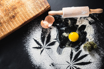 The process of making cannabis pastries. raw broken egg, a rolling pin, flour, and dried marijuana inflorescences.