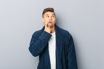 Young caucasian man wearing pajama looking sideways with doubtful and skeptical expression.