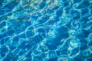 Fototapeta na wymiar Wavy blue water in an outdoor pool or fountain on a bright sunny day