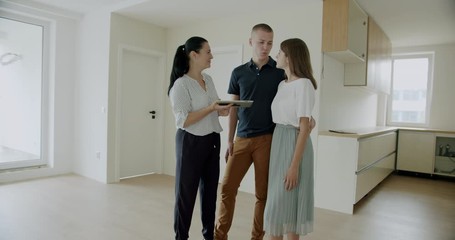 First time buyers electronically signing digital tablet in new house. Young couple buying their first home signing a contract on a digital tablet.