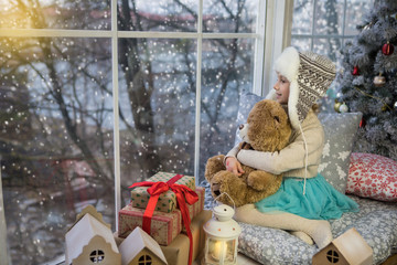 Little girl sitting by the window with a bear