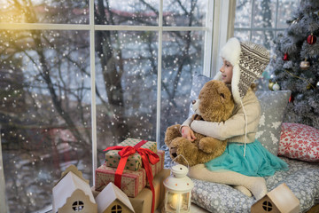 Fototapeta premium Little girl sitting by the window with a bear