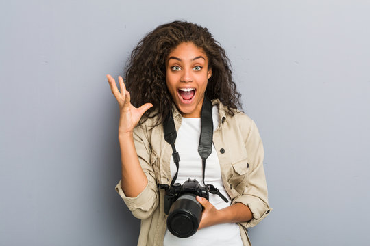 Young african american photographer woman holding a camera celebrating a victory or success