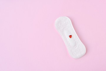Daily soft cotton pad with red decorative heart on pink background with empty space for text. Menstrual pad. Women's health concept monthly period days. Woman critical days, menstruation cycle 
