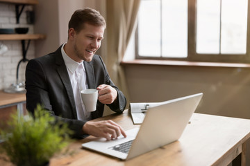 happy handsome business man checking mail in laptop and reading magazine in the kitchen while drinking hot tea before going to work . multitasking, morning