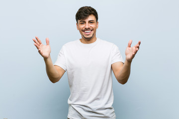 Young caucasian man wearing a white tshirt receiving a pleasant surprise, excited and raising hands.