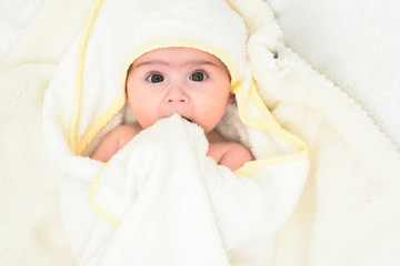 Adorable 6 months old Baby girl infant on a bed on her belly with head up looking into camera with her big eyes. Natural light.