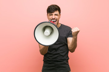 Young hispanic man holding a megaphone cheering carefree and excited. Victory concept.