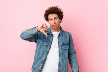 Curly mature man wearing a denim jacket against pink background showing a dislike gesture, thumbs...