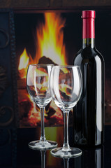Bottle of wine and two empty glasses on the background of the fireplace.