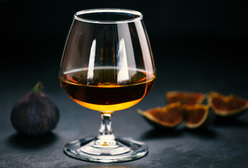 Whiskey or cognac in a glass and figs on dark concrete