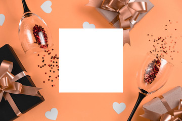 Holiday background. Two clinking wine glasses, various handmade gift boxes decorated with pink heart confetti, white frame on orange background. Valentines day concept. Flat lay, top view, copy space