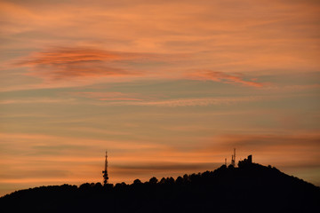 Silhouette of a telecommunications tower and another historic stone on a hill at sunset