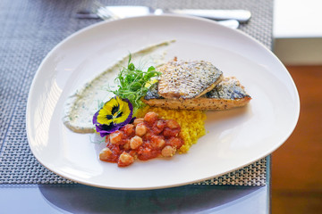 Closeup perfectly executed mullet fillet steak with crispy fish skin, couscous and chickpeas on table in restaurant. Plate with dish of mullet fish.