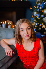 Beautiful happy young woman sits by a chair in the New Year decor.