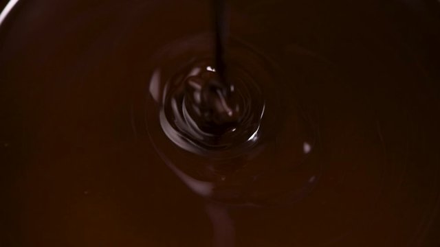 Liquid dark chocolate mixing with golden spoon. Closeup view
