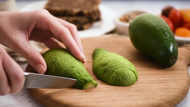 Chef slicing avocado on a wooden cutting board. Healthy vegan cooking