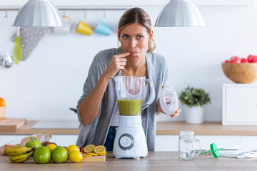 Pretty young woman tasting the detox juice she just made with the blender at home.
