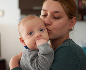 Pretty woman holding a three months baby with blue eyes in her arms